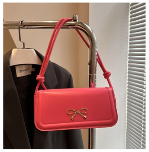 Détail d'un sac baguette rose vif avec un nœud doré et une bandoulière à nœuds élégante