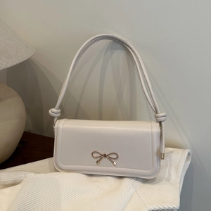 Détail d'un sac à bandoulière crème avec nœud doré sur tissu rayé doux