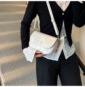 Detail of white glossy crossbody bag featuring silver metal clasps and round button flap