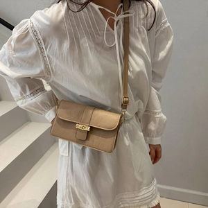 Elegant beige croc-pattern shoulder bag with gold metal clasp on a minimalist model