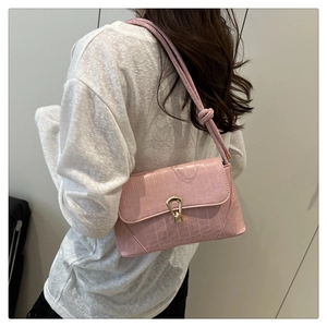 Detail view of pink crocodile embossed leather bag with a gold horseshoe clasp and knotted strap