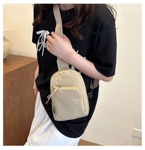 Compact beige canvas chest bag worn across the body with adjustable strap and dual zippers