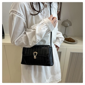 Detail of black crocodile-embossed leather bag with elegant gold horseshoe buckle