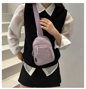 Close-up of a light purple nylon crossbody bag worn by a model in a casual indoor setting
