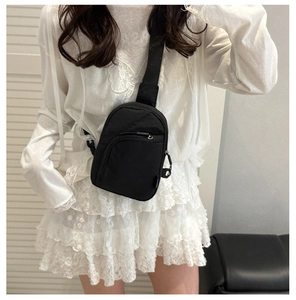 Lifestyle shot of a black nylon crossbody chest bag worn over a white lace top