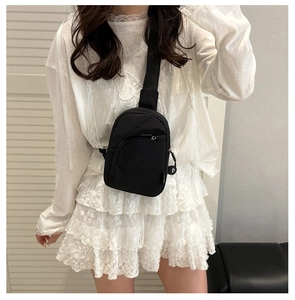 Gros plan d'un mini sac bandoulière en nylon noir porté avec une tenue en dentelle blanche