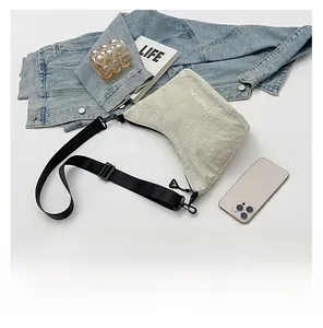 Detail showing beige nylon pleated crossbody bag with FASHION logo and black strap