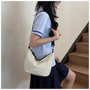 Detail of a minimalist cream nylon dumpling bag with black strap and fashion print