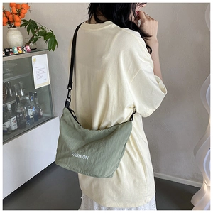 Detail of green crescent nylon bag with adjustable black strap worn over the shoulder