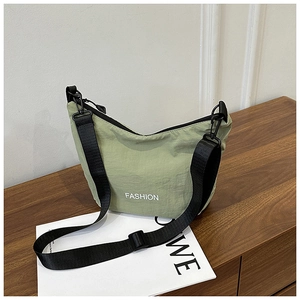 Detail view of green nylon dumpling bag with black strap on a wooden surface