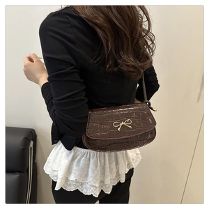 Dettaglio borsa baguette marrone effetto coccodrillo con elegante fiocco dorato