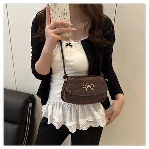 Dettaglio mini borsa in pelle coccodrillo marrone scuro con fiocco dorato indossata