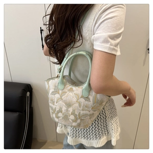 Exquisite floral embroidery detail on cream handbag with green strap shown on model