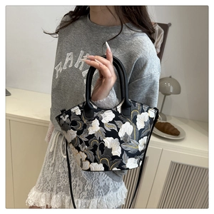 Détail de broderie florale sur un sac en tissu noir avec poignée ronde et bandoulière