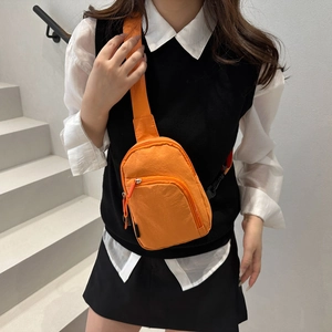 Orange nylon crossbody sling bag with adjustable strap shown on a model in street style