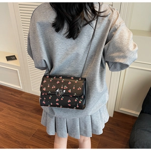 Chic black crossbody bag with red cherry prints and metal chain strap on a model