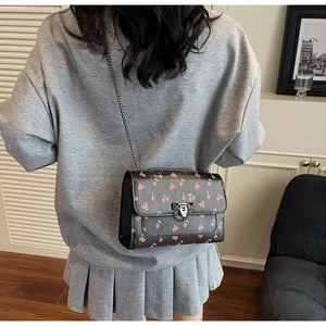 Détail du sac bandoulière noir avec imprimés cerises et chaîne porté par un mannequin