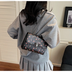 Détail du sac bandoulière noir à motif cerise avec chaîne dorée dans un décor de style de vie