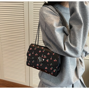 Detail of crossbody bag with cherry print, silver metal clasp and chain strap on model