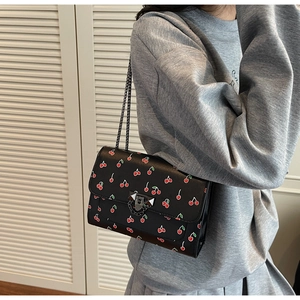 Close-up of cherry print crossbody bag featuring dark metal chain and twist lock detail