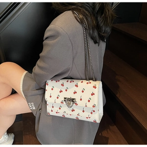 Détail du sac bandoulière blanc à imprimé cerises et bandoulière chaîne argentée