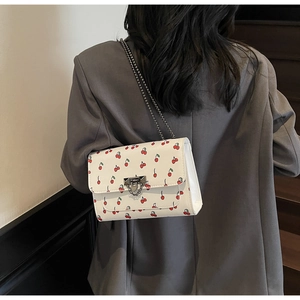 Détail du sac à bandoulière blanc à motif cerise avec chaîne en métal et fermoir doré