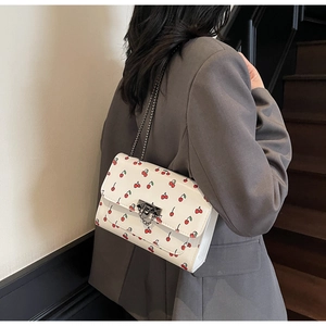 Close-up of cherry print crossbody bag with charcoal metal clasp on a gray blazer