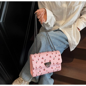 Detail of pink cherry print crossbody bag with silver pyramid stud lock and chain strap