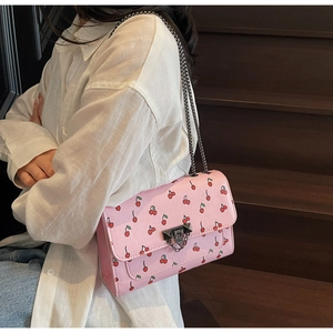 Sac bandoulière rose à imprimé cerise avec chaîne métallique porté de côté par un mannequin