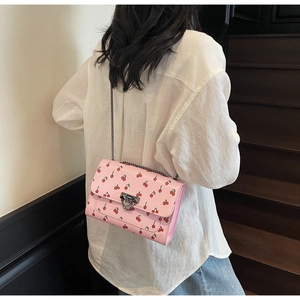 Détail du sac à bandoulière rose avec imprimé cerise et chaîne dorée sur un mannequin