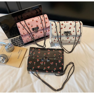 Three cherry print crossbody bags in pink, white, and black with metal chain straps