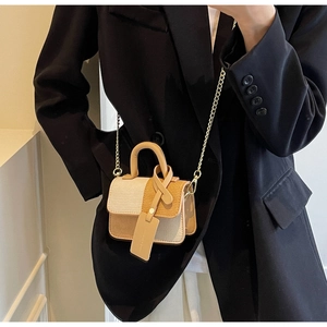 Detail of contrast color mini crossbody bag with gold chain strap on black blazer