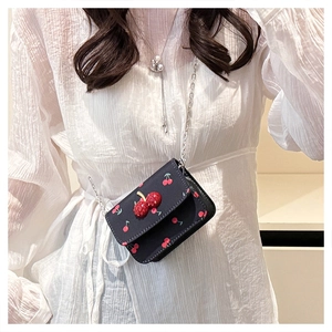 Détail du sac bandoulière bleu marine à imprimé cerise et breloque strass sur un modèle