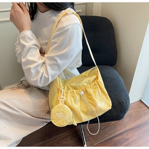 Detail der gelben Nylon-Umhängetasche mit Kordelzug und kreisförmigem Mini-Taschenanhänger