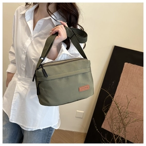 Détail du sac bandoulière en nylon vert olive montrant le logo en cuir et la fermeture