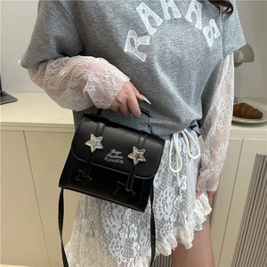 Chic black square handbag with silver star buckles and shoulder strap worn by a model