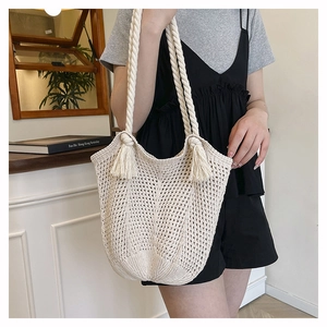 Detailed close-up of beige crochet knit tote bag with tassel accents and woven handles