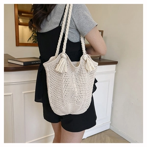Close-up of beige knit tote bag with macrame knot details and boho tassel accents