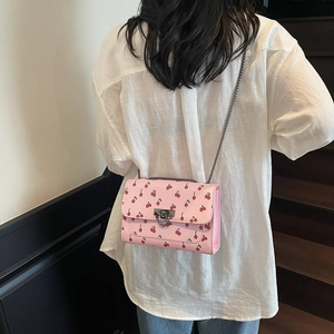 Pink crossbody bag with cherry print and metal chain strap shown on a model