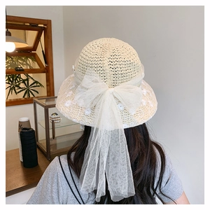 Detail of elegant beige straw sun hat with large mesh bow, pearls, and floral embroidery