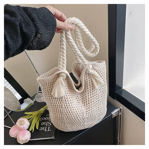 Detailed close-up of beige crochet bucket bag with braided rope handle and tassel detail