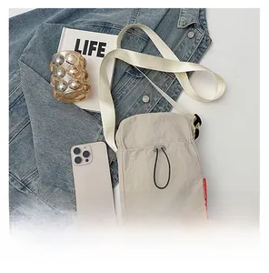 Detail view of beige nylon crossbody phone bag with drawstring pocket and woven strap