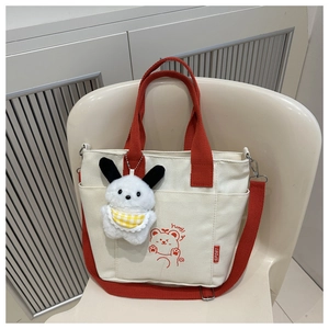 Detail view of the beige canvas tote bag featuring a cute red bear print and plush charm