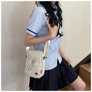 Close-up of cream nylon crossbody bag featuring a drawstring pocket and red label detail