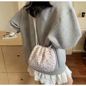 Detail of floral drawstring bucket bag worn cross-body in a cozy indoor setting