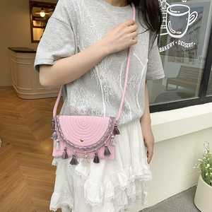 Pink woven saddle bag with tassel accents and gold buckle shown on a female model