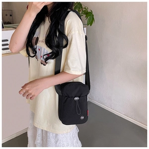 Close-up of minimalist black nylon crossbody bag with drawstring pocket and wide strap