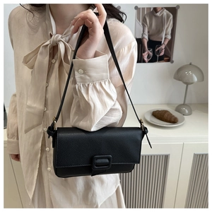 Detail of minimalist black lychee textured PU leather baguette bag with square buckle strap