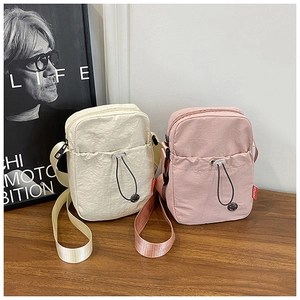 Detail of compact nylon crossbody bags in cream and pink with adjustable straps