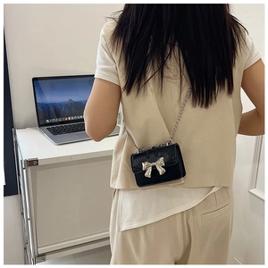 Detail of a mini black crossbody bag with silver bow buckle and chain strap on person